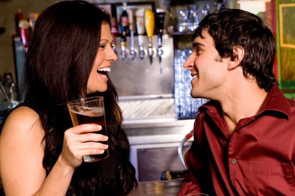 o femeie cu un pahar de bere in mana care zambeste in fata unui barbat care zambeste intr-un bar