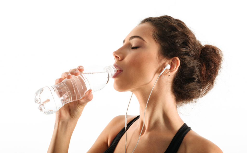 femeie care bea apa din sticla si are casti in urechi