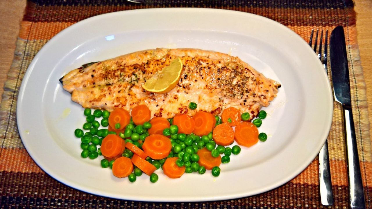 prepared fish next to carrots and peas on a plate