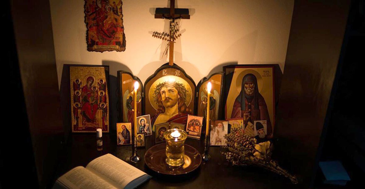 altar de icoane, cu o lumanare aprinsa si o carte de rugaciuni deschisa