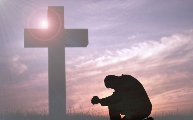 persoana care se roaga cu o cruce in fundal
