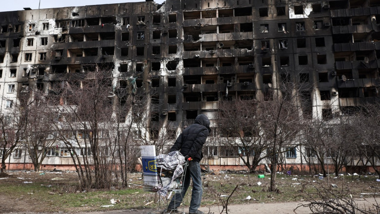 Mariupol după o lună de război, barbat ucrainean ce trage un carucior dupa el in zona unor blocuri distruse de bombardamentele armatei ruse
