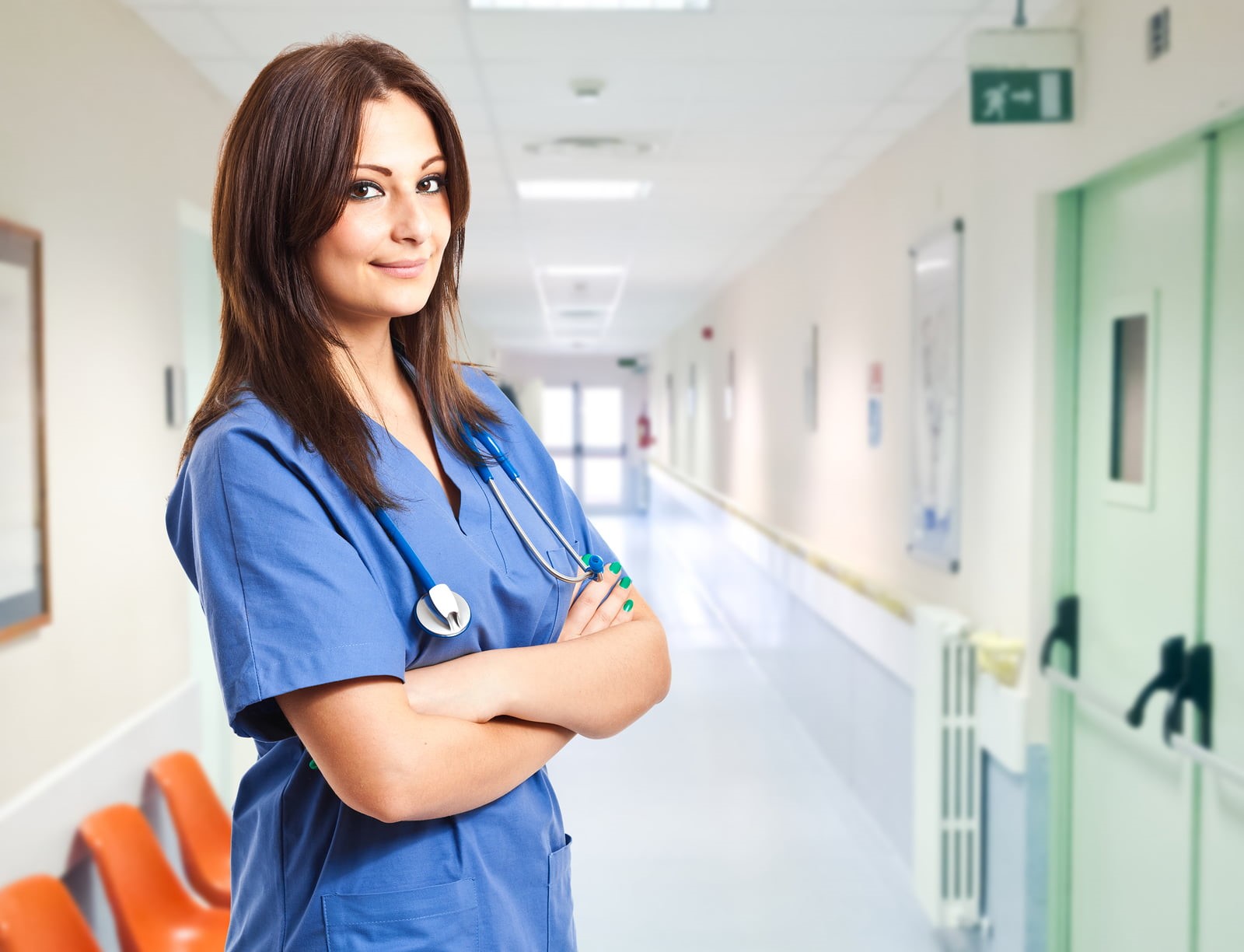 o asistenta medicala, imbracata in compleu albastru, sta pe holul unui spital