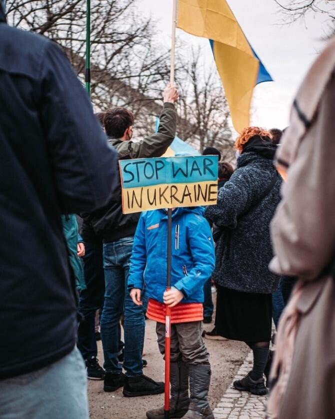 o multime care protesteaza si un copil care tine in manao panacarda pe care scrie stop razboi in ucraina