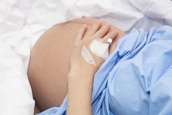 o femeie însărcinată pe patul de spital cu branulă la mână