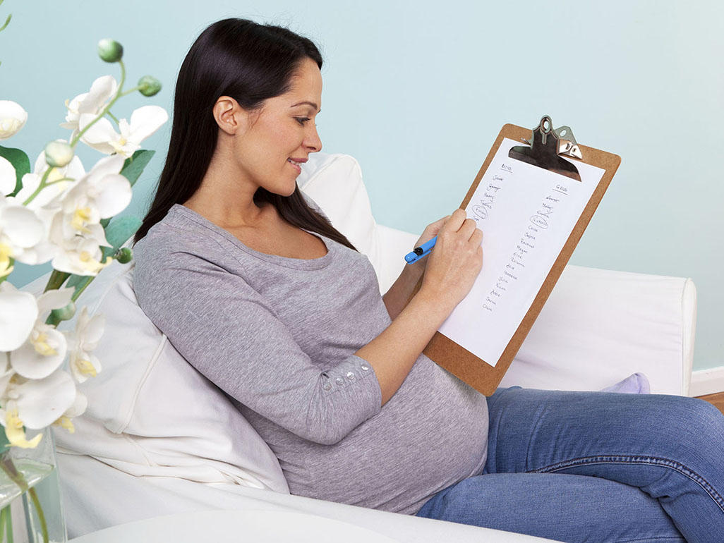o femeie însărcinată care pregătește lista pentru bagajul de maternitate