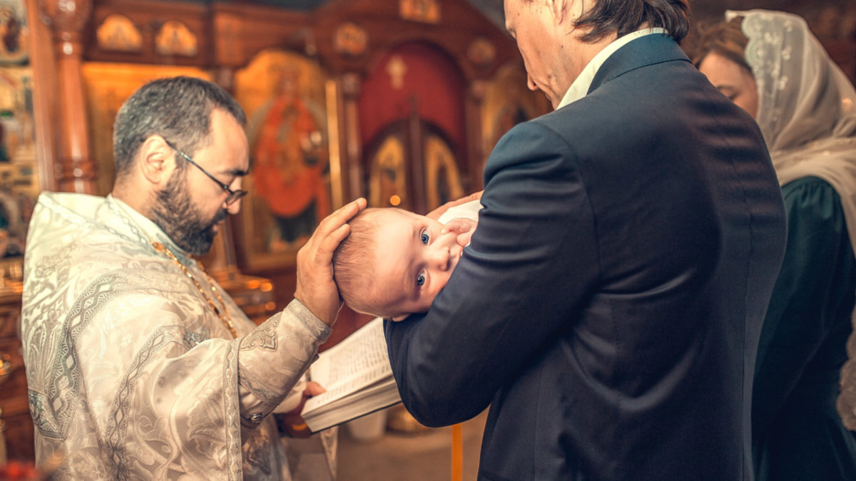 pereche de nasi care tin in brate un bebelus in timpul botezului