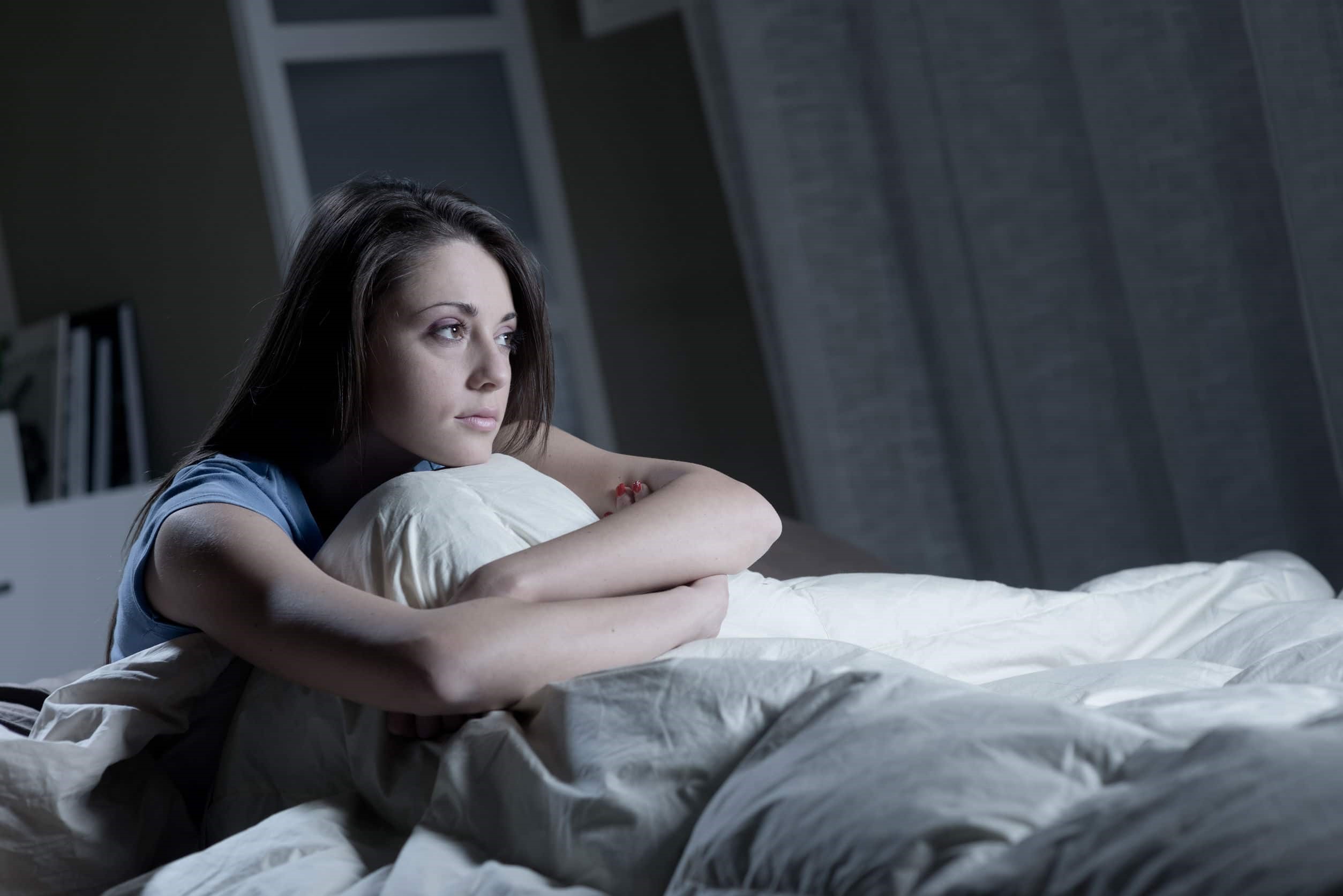 femeie care sta asezata pe pat noapte si priveste ingandurata