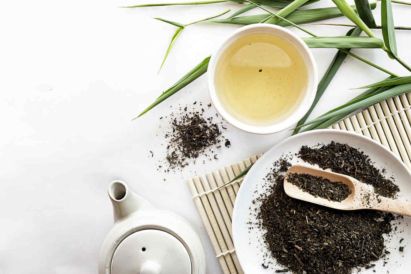 o cana cu ceai detoxifiant langa o farfurie cu plante uscate si un ceainic pe o masa