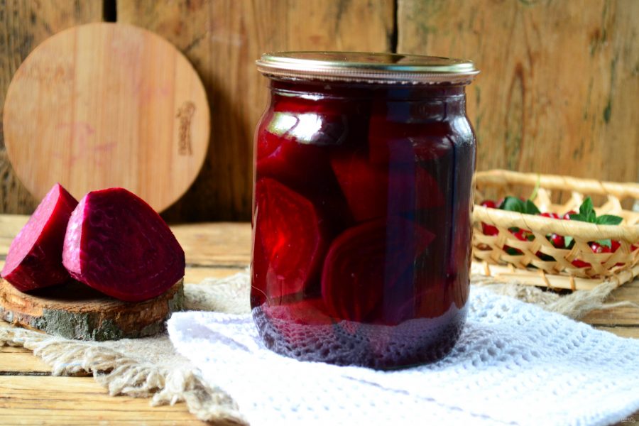 A jar of pickled red beets next to a few beet slices on the table