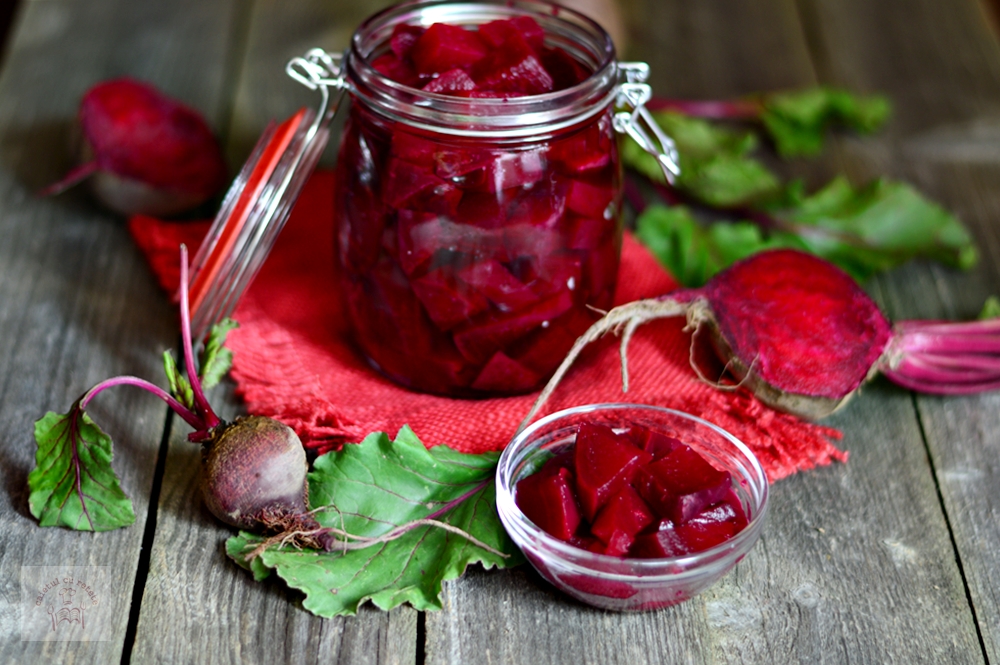 An open jar of beetroot next to a few beet leaves and a small bowl of beetroot pieces