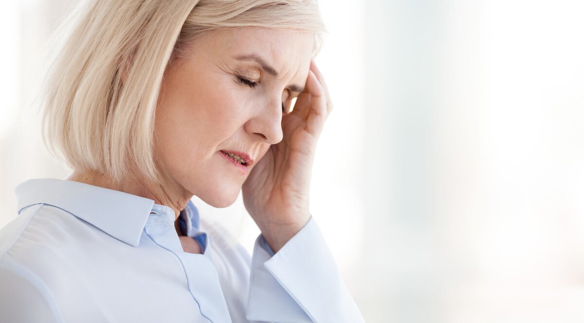 femeie care sufera de dureri de cap si se tine de el din cauza menopauzei